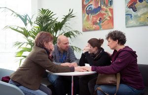 Gruppe sitzt um Tisch und hält die Hände