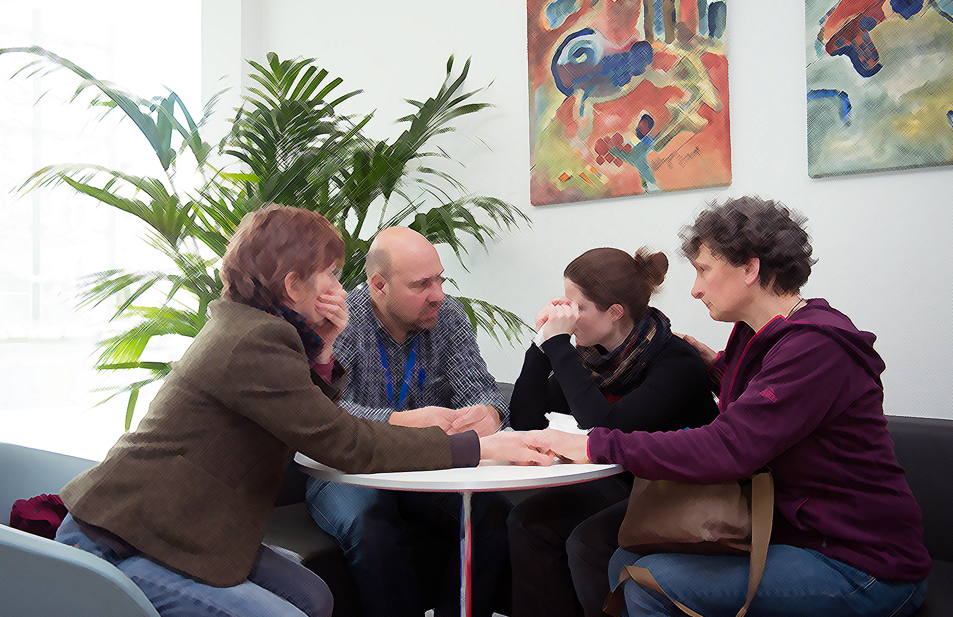 Gruppe sitzt um Tisch und hält die Hände