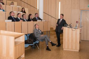 Mann an Rednerpult in Hörsaal vor Publikum