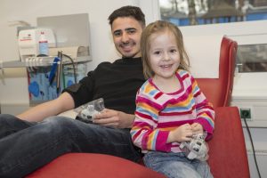Junger Mann beim Blutspenden mit Kind neben sich