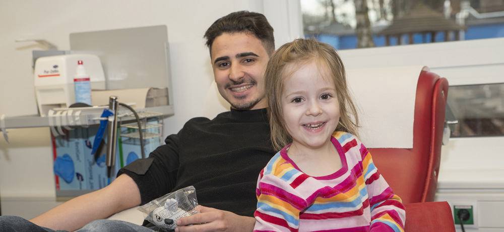 Junger Mann beim Blutspenden mit Kind neben sich