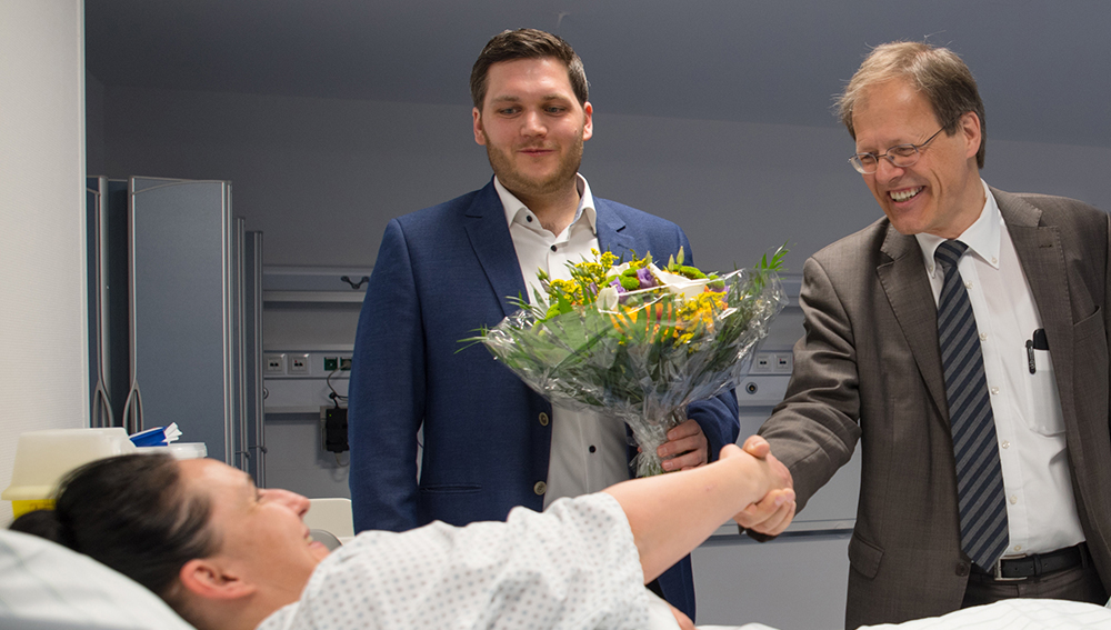 Prof. Wolfgang Holzgreve, Ärztlicher Direktor und Vorstandsvorsitzender am UKB, und Thorsten Trinks, OP-Koordinator am UKB, begrüßen die erste Patientin bei der offiziellen Inbetriebnahme der Patientenholding Area am UKB.