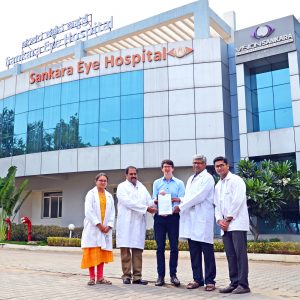 Dr. Maximilian Wintergerst (Mitte) präsentiert zusammen mit den Kollaborationspartnern des Sankara Eye Hospital in Bangalore Dr. Kaushik Murali (2. v. li), Dr. Mahesh Shanmugam (2. v. re), Dr. Divyansh Mishra (1. v. re) und Dr. Payal Shah (1. v. li) den Fördervertrag