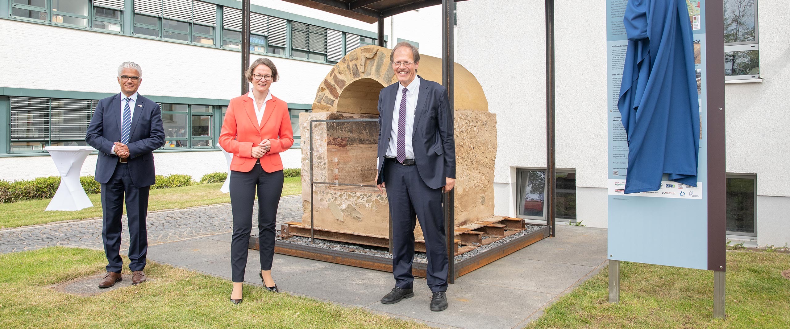 Oberbürgermeister der Bundesstadt Bonn Ashok Sridharan, Ina Scharrenbach, Ministerin für Heimat, Kommunales, Bau und Gleichstellung des Landes Nordrhein-Westfalen, und Prof. Wolfgang Holzgreve, Ärztlicher Direktor und Vorstandsvorsitzender am UKB, vor der römischen Wasserleitung am Institut für Hygiene und Öffentliche Gesundheit am UKB