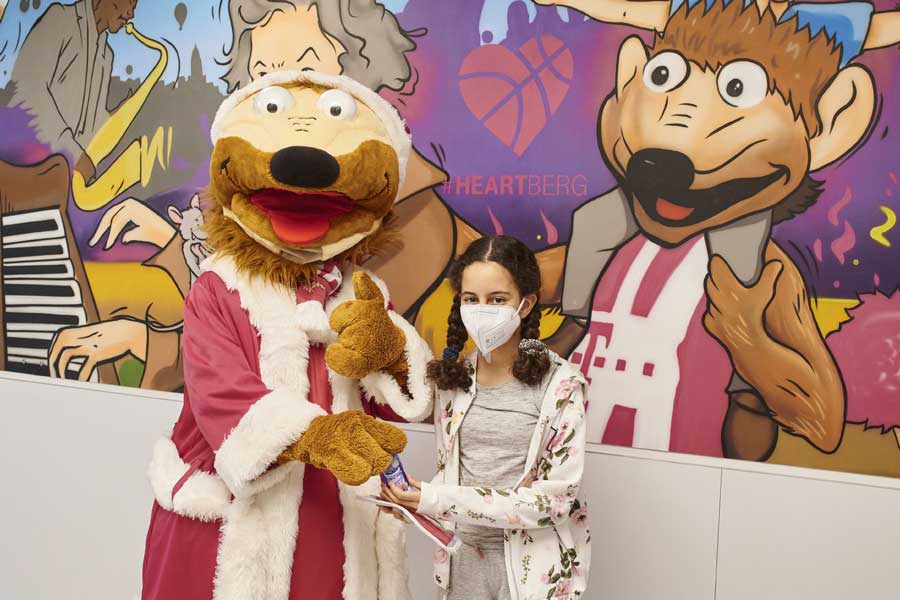 Maskottchen Bonni der Telekom Baskets Bonn schenkt der kleinen Amira, Patientin im ELKI des UKB, einen Schokonikolaus und eine Kinderalltagsmaske. 