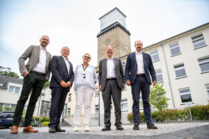 Urs Reitis, Geschäftsführer der Bonn-Netz GmbH, Theo Waerder, Geschäftsführer der Versorger-Allianz 450 Beteiligungs GmbH & Co. KG, Charlotte Kaspari, Leiterin des Geschäftsbereichs Gebäudemanagement am UKB, Prof. Wolfgang Holzgreve, Ärztlicher Direktor und Vorstandsvorsitzender des UKB und Sebastian Rötzel, Projektleiter Ausbaugebiet Mittelrhein (v.l.n.r.), stehen vor dem ukb-Turm, auf dem der Funkmast befestigt ist.